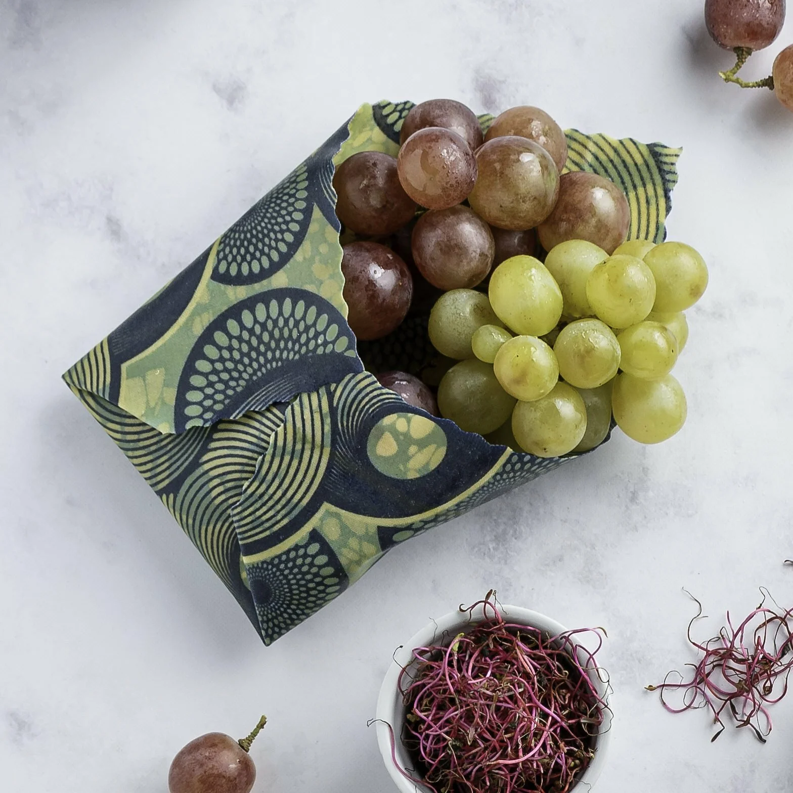 Bee wrap taille Small collection "Air marin" de L'abeille qui emballe, formant une enveloppe autour de raisins frais
