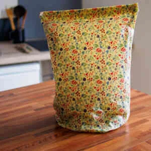 Sac à pain en cire d'abeille (motif petites fleurs bleues) fermé et contenant une baguette et un pin tranché
